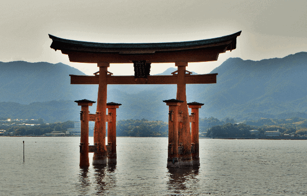 The orange Torii gate of Itsukushima Shrine with the sun setting behind it