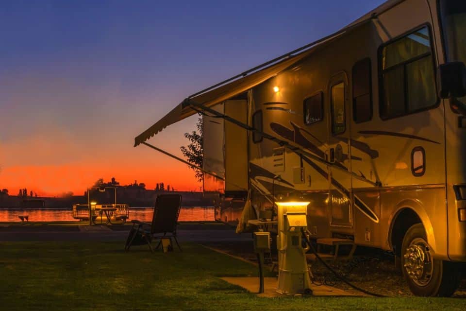 A motorhome parked next to a lake with a bright orange sunset in the background