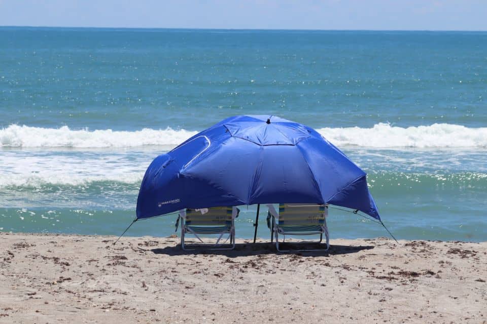 Two beach chairs facing the ocean, shielded by a blue tent