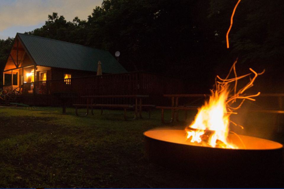 A campfire at night with a lighted cabin in the background