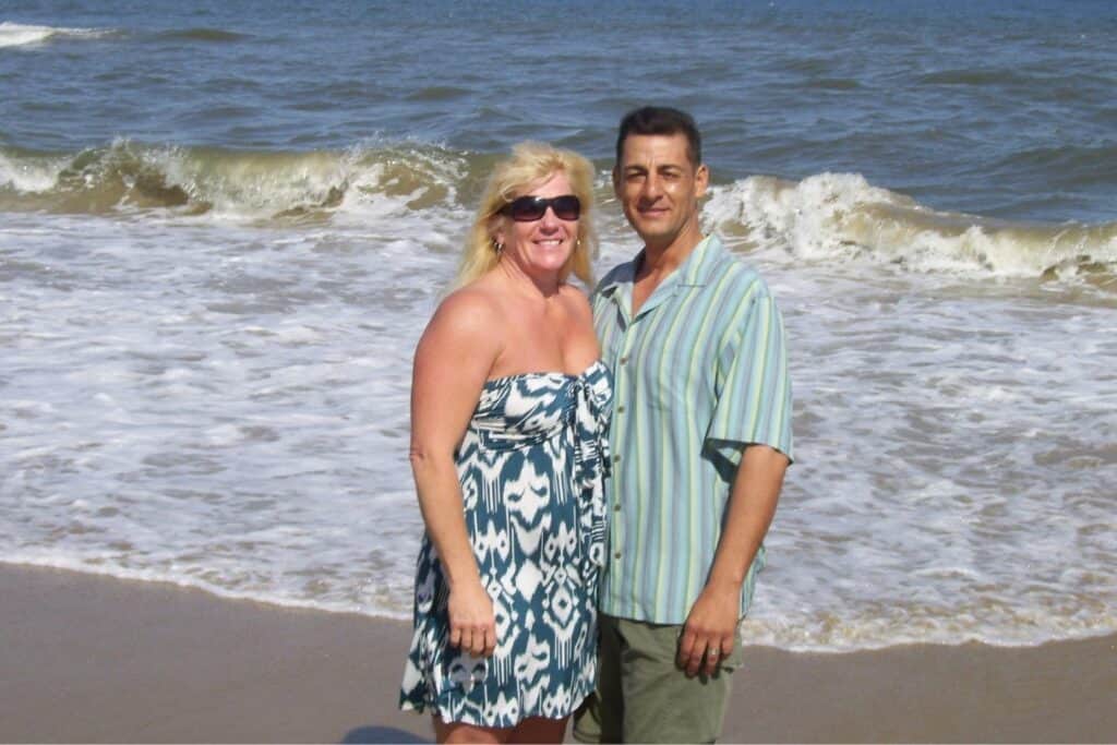 a couple standing on the beach with the ocean behind them