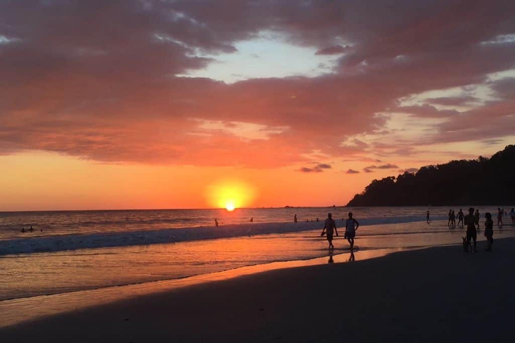 Sunset at a beach with silhouettes of people walking along the shore