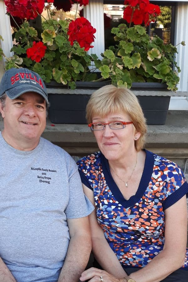 a retired couple sitting together with flowers behind them