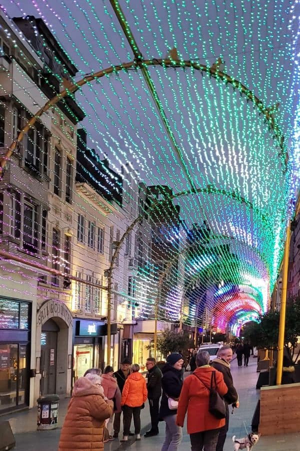 A busy pedestrian street with strings of colored lights overhead