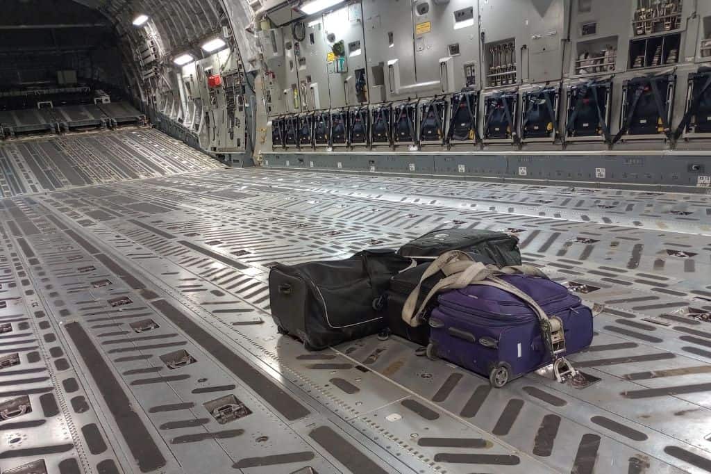 the inside of a military cargo plane with a few suitcases strapped down in the center