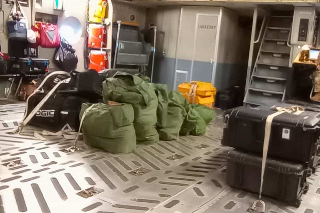 the inside of a military cargo aircraft with bags strapped to the floor