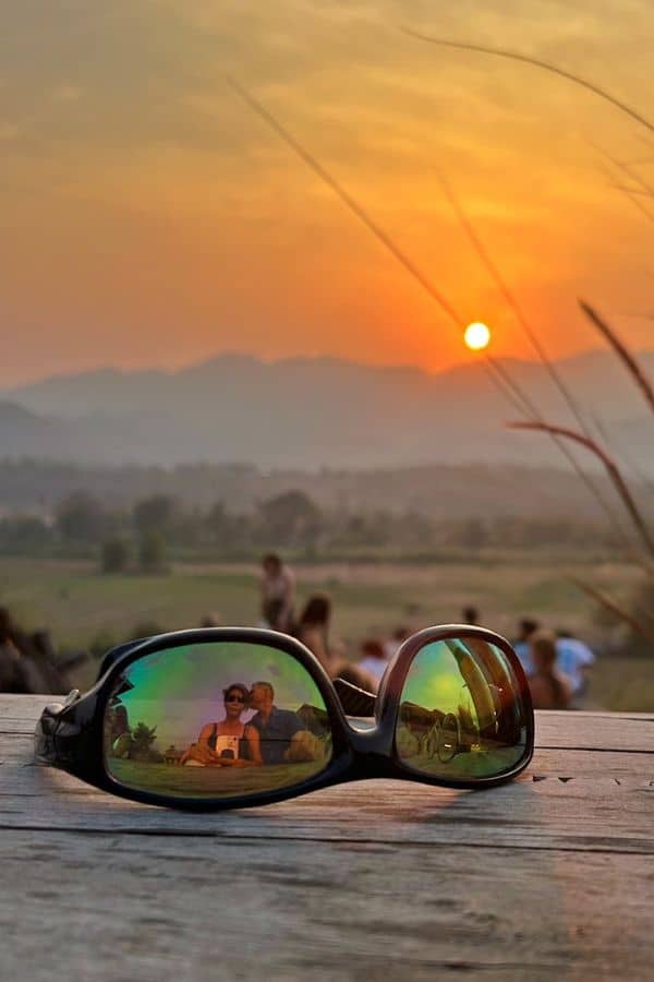 a pair of sunglasses on a table with a sunset in the background. 