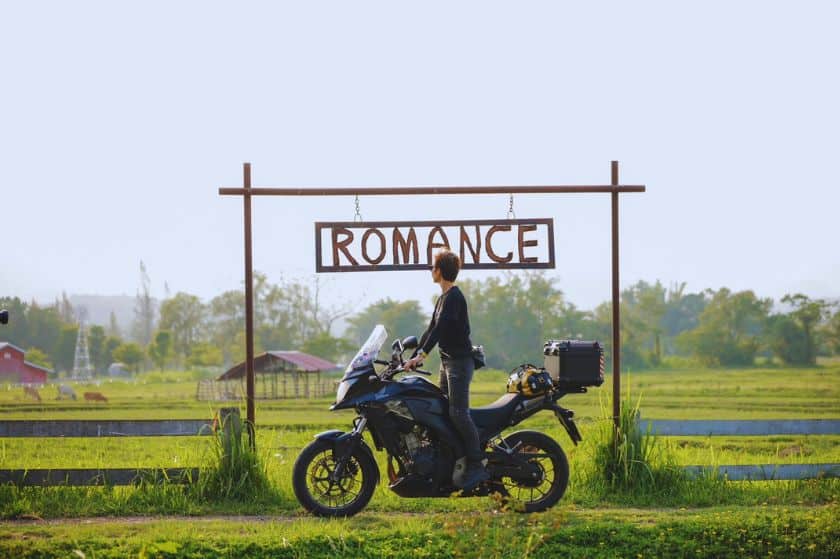 a woman standing up on a motorcycle in front of a sign that says "romance"