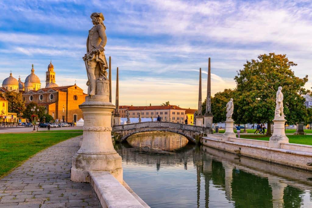 a canal lined with white statues and a basilica in the background