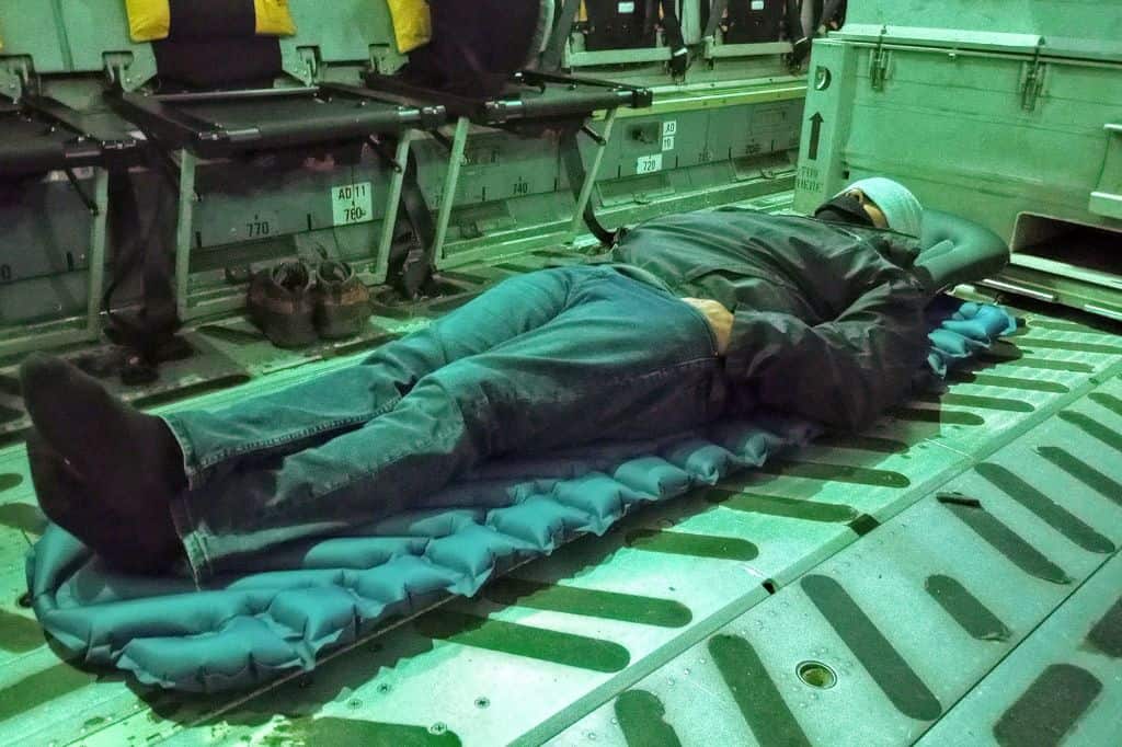 a man lying on an inflatable mat on the floor of a cargo airplane