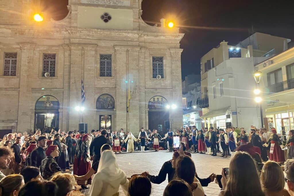 people join hands for a traditional greek dance in front of a cathedral