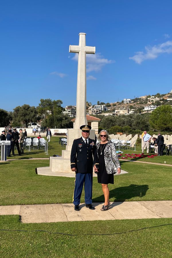 a couple standing in front of a statue of a cross. the man is in a military dress uniform