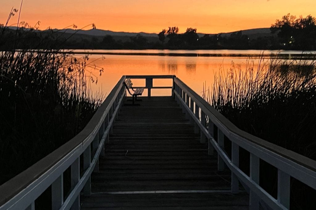 A boardwalk leading out to a calm lake at sunset