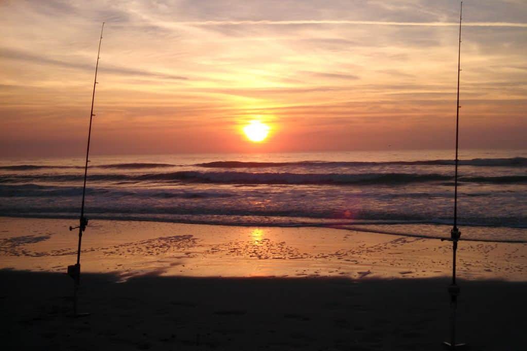 Two fishing poles in the sand at sunset