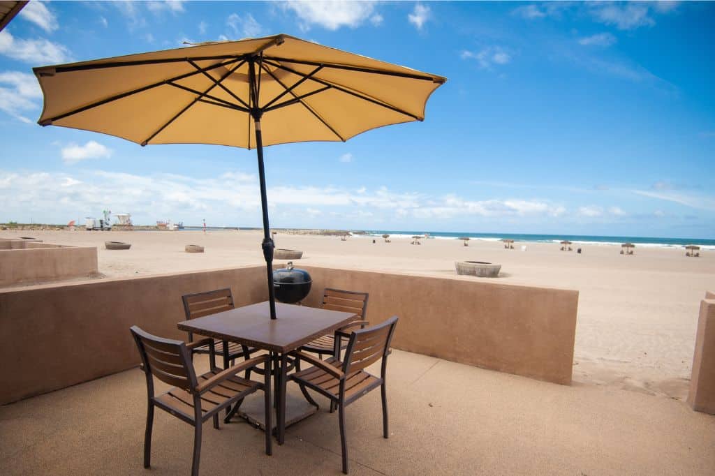 A patio with table, chairs and umbrella located directly next to the beach