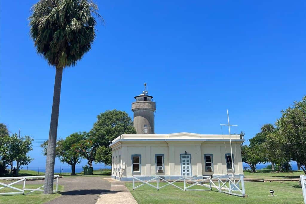 Lighthouse with a white building in front, palm tree, and ocean view