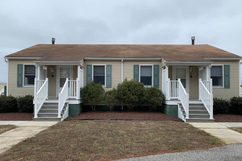 Beige duplex with porches, green shutters, and trimmed bushes