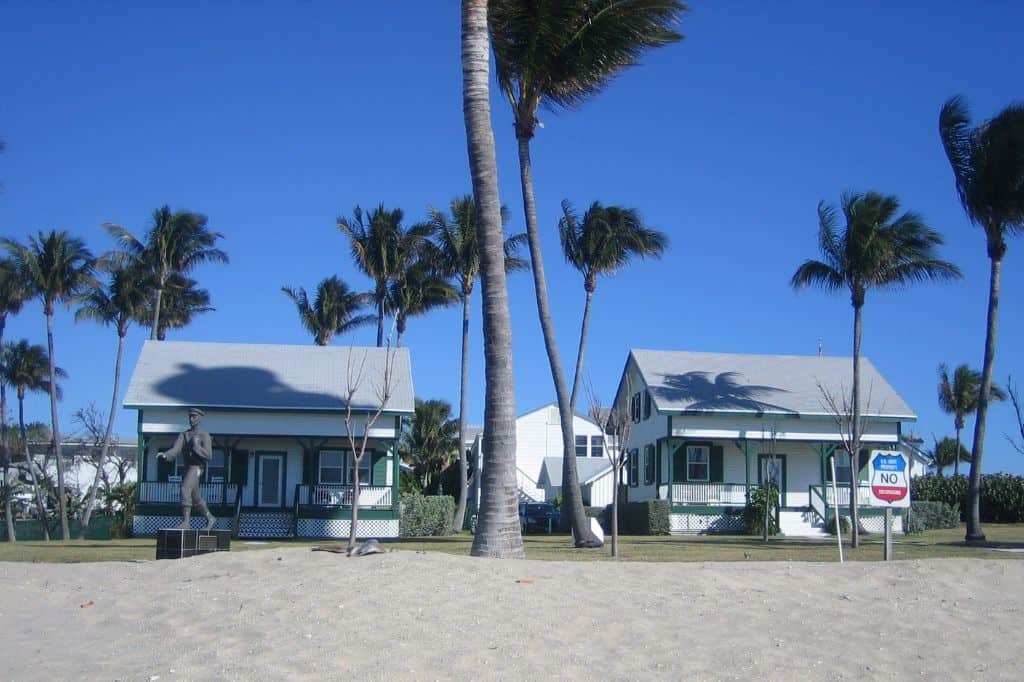 White cottages with green trim near a sandy beach and palm trees