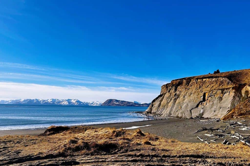 Coastal cliffs overlooking a dark sand beach with distant mountains