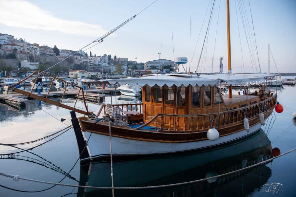 A traditional wooden boat with a canopy docked in a marina, with a European coastal town in the background.