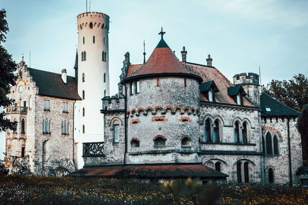 A grand European castle with intricate architecture, turrets, and a tall tower, set against a soft blue sky.