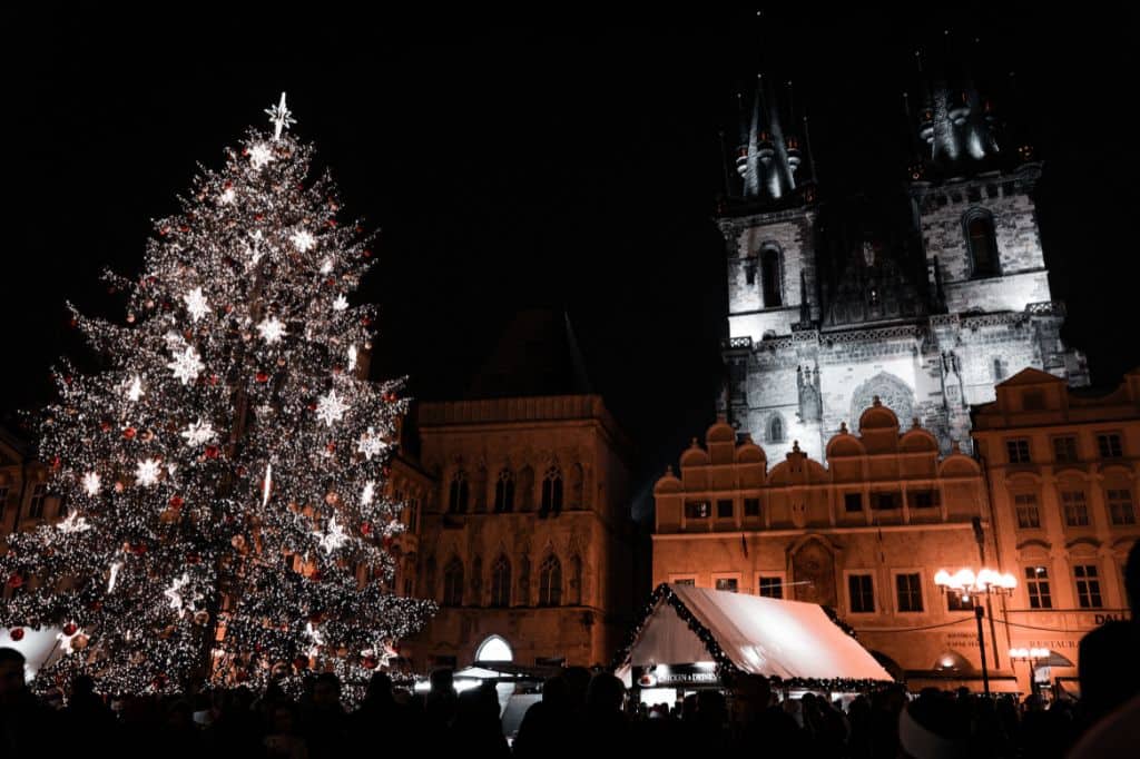 A festive Christmas market at night, featuring a large illuminated Christmas tree and a historic cathedral in the background.