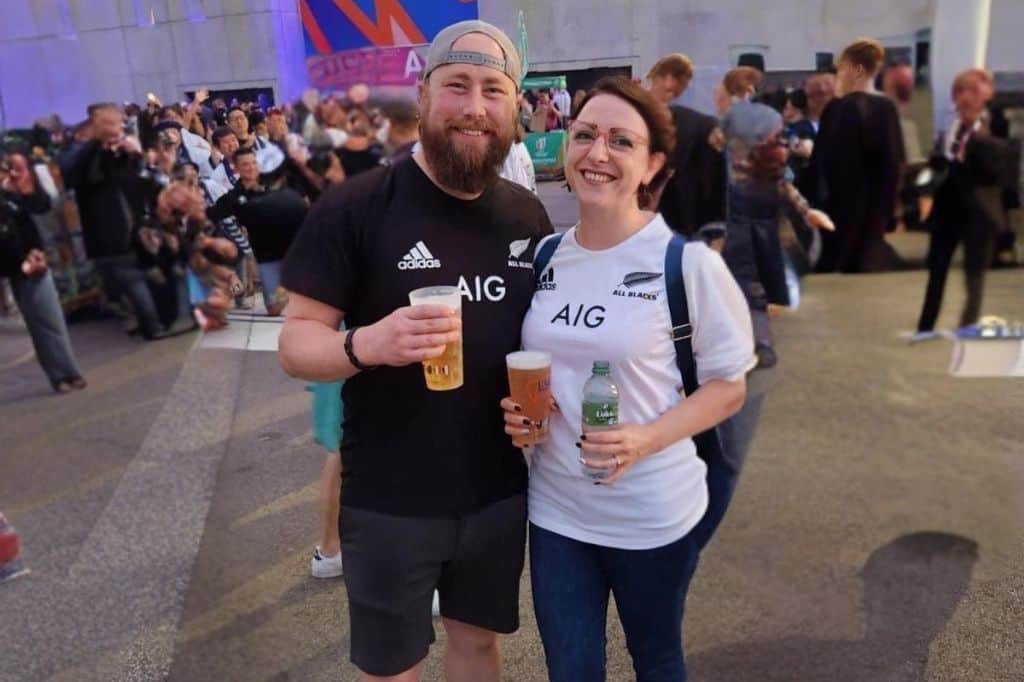 a man and a woman smiling, holding beers at an event