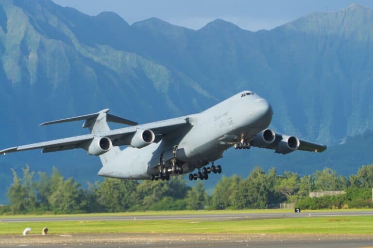 military cargo plane taking off with mountains in the background